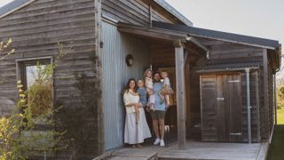 A family of five with 3 young children stand at the entrance to a Cotswold Farm Park Holidays lodge with the children held in their arms